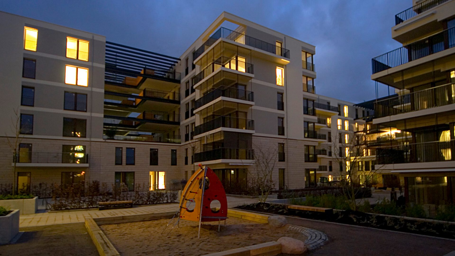 Die Clarenbach Gärten am Abend mit beleuchteten Wohnungen und Spielplatz