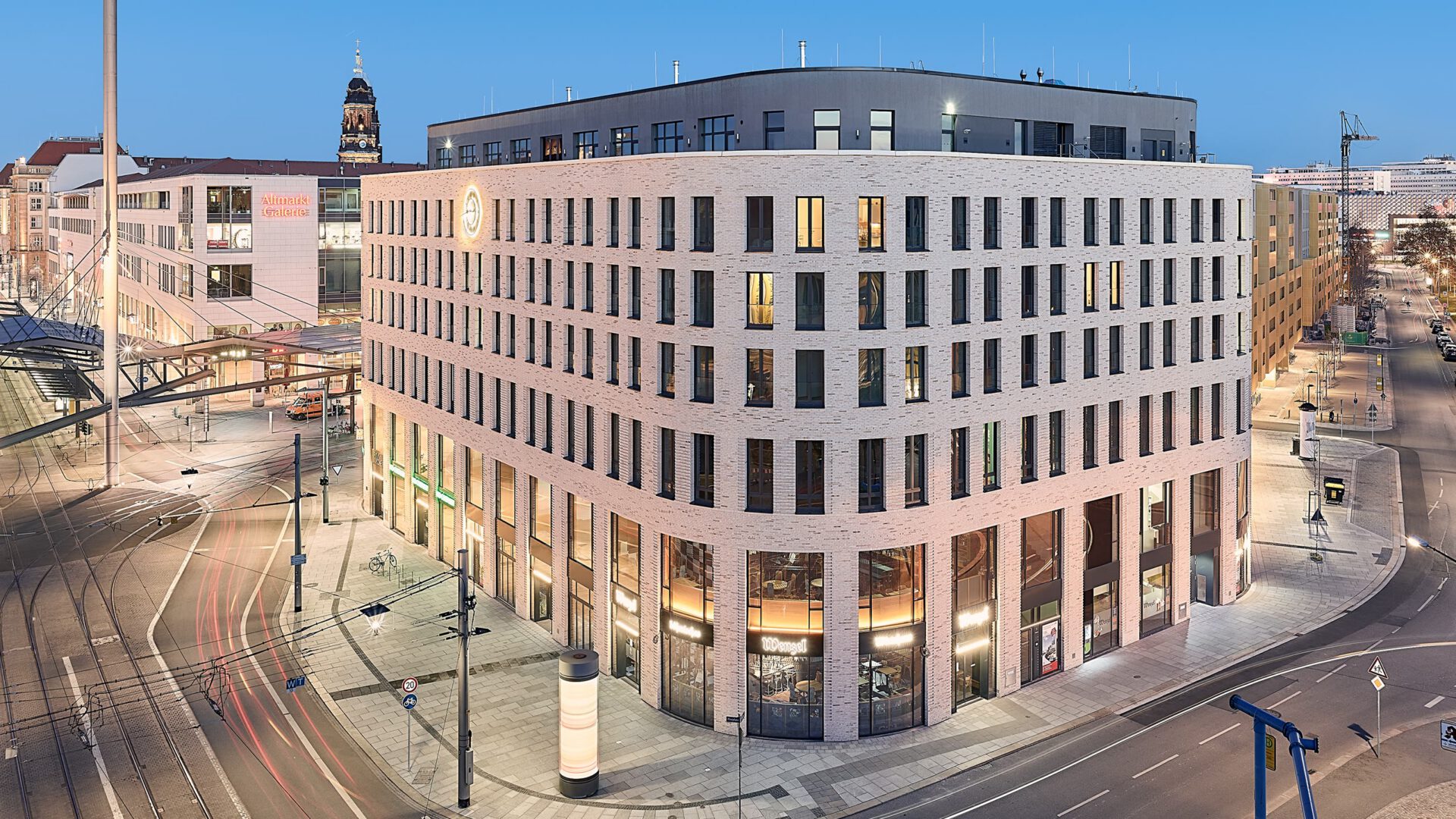 HAUS POSTPLATZ in der Dämmerung, davor die Gleise am Postplatz