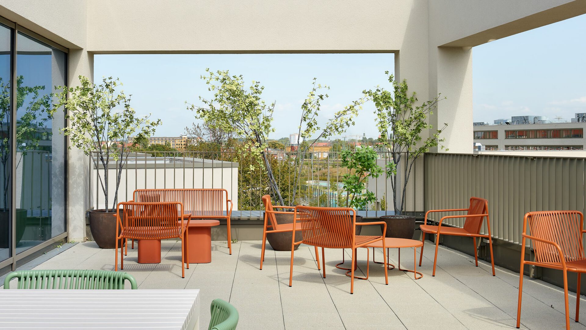 Gedeckte Dachterrasse mit orangefarbenen Sitzmöbeln und Blick über Leipzig