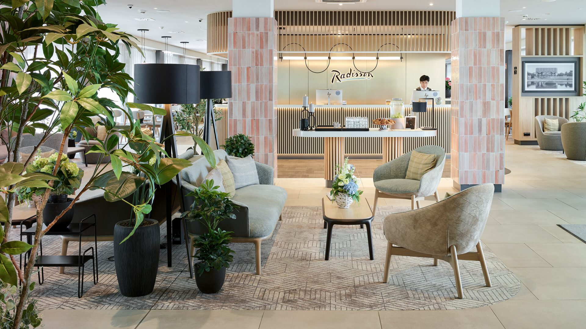 Hotellobby mit Sitzgruppen, Pflanzen und der Rezeption im Hintergrund