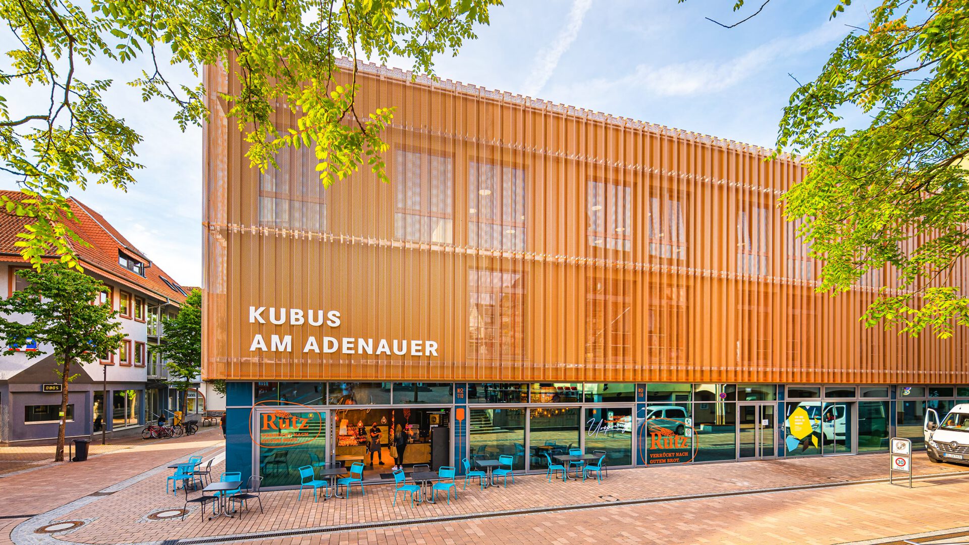 KUBUS AM ADENAUER in ganzer Breite, gerahmt von den Bäumen der Fußgängerzone