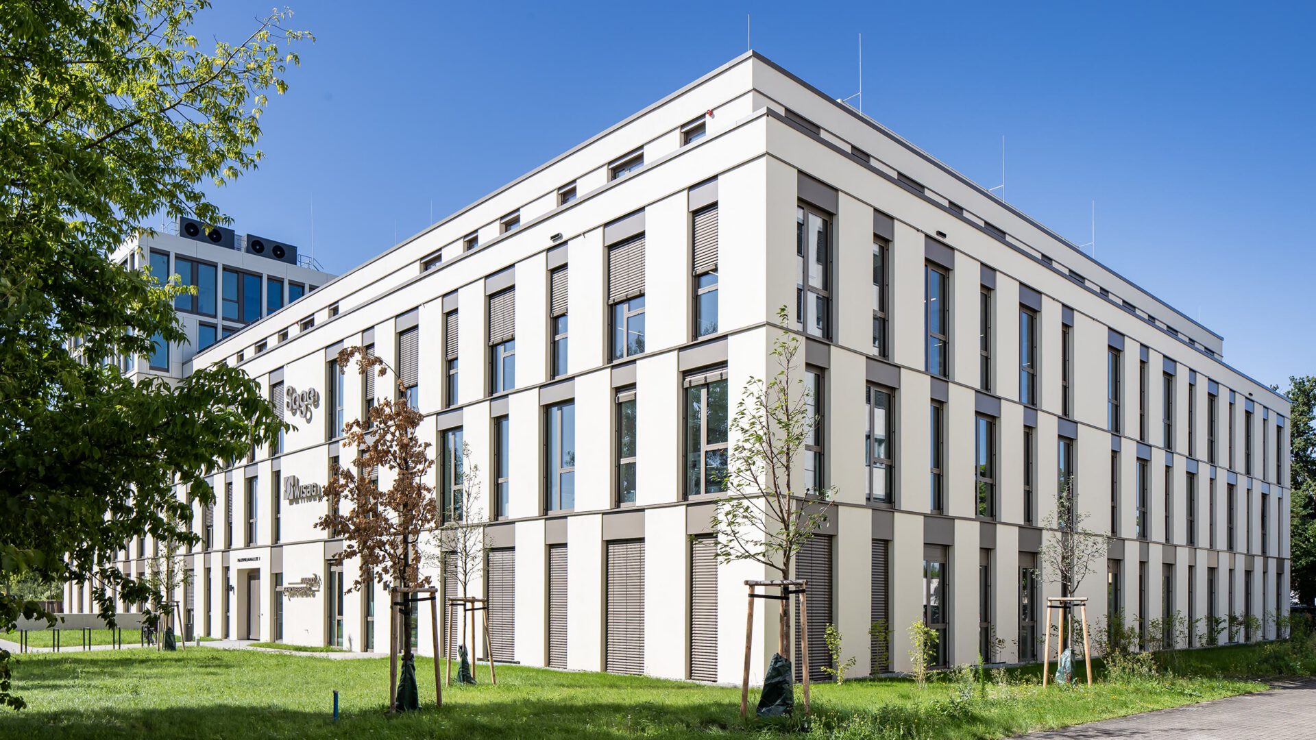 Gebäudeecke von MITZSCH mit gerasterter Lochfassade und begrünter Vorfläche