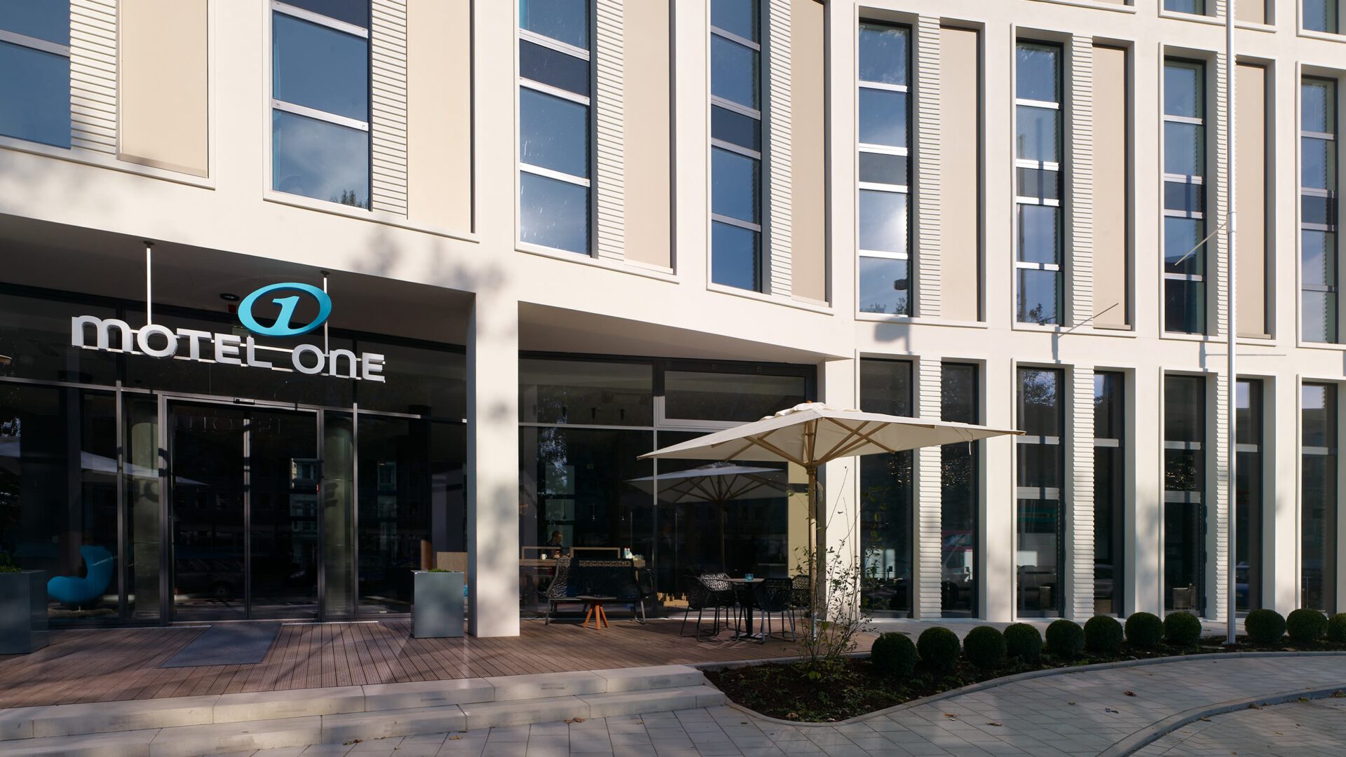 Eingang des Motel One mit Terrasse und Sonnenschirm
