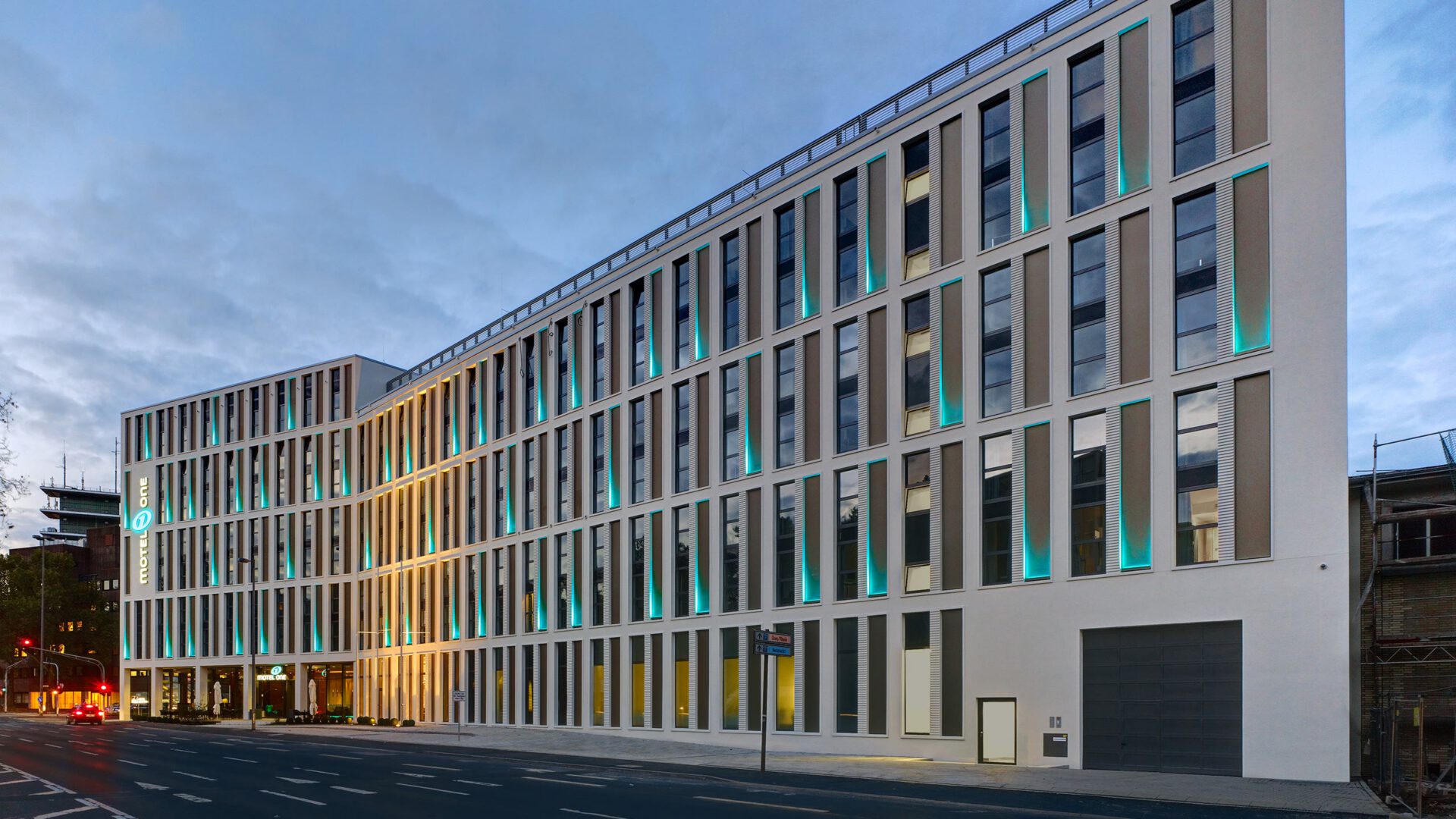 Motel One am Abend mit türkis beleuchteten Fassadenfugen