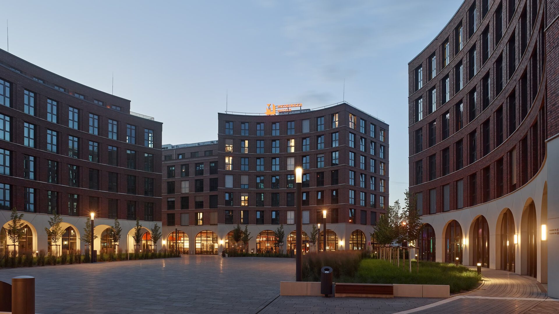Abendaufnahme von OVUM mit beleuchtetem Meininger-Hotel im Hintergrund