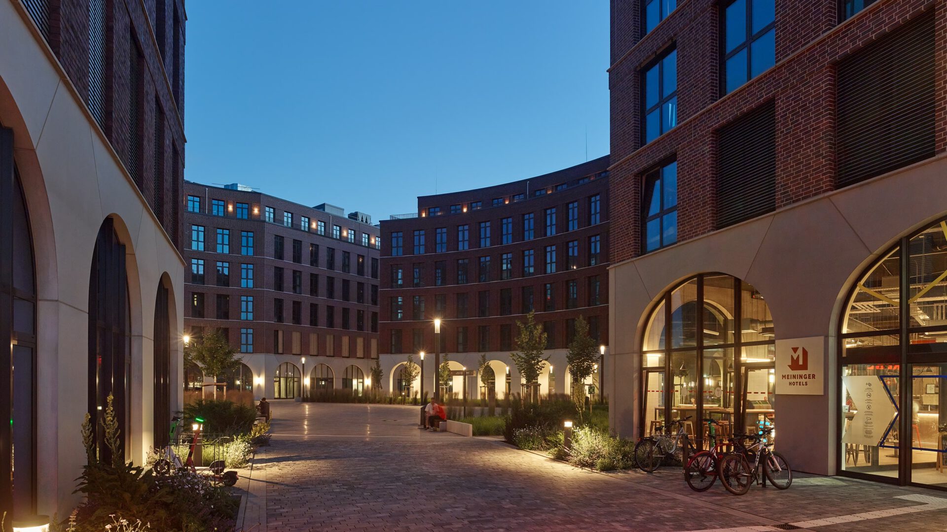 Beleuchtete Quartiersgasse von OVUM bei Nacht mit Läden im Erdgeschoss